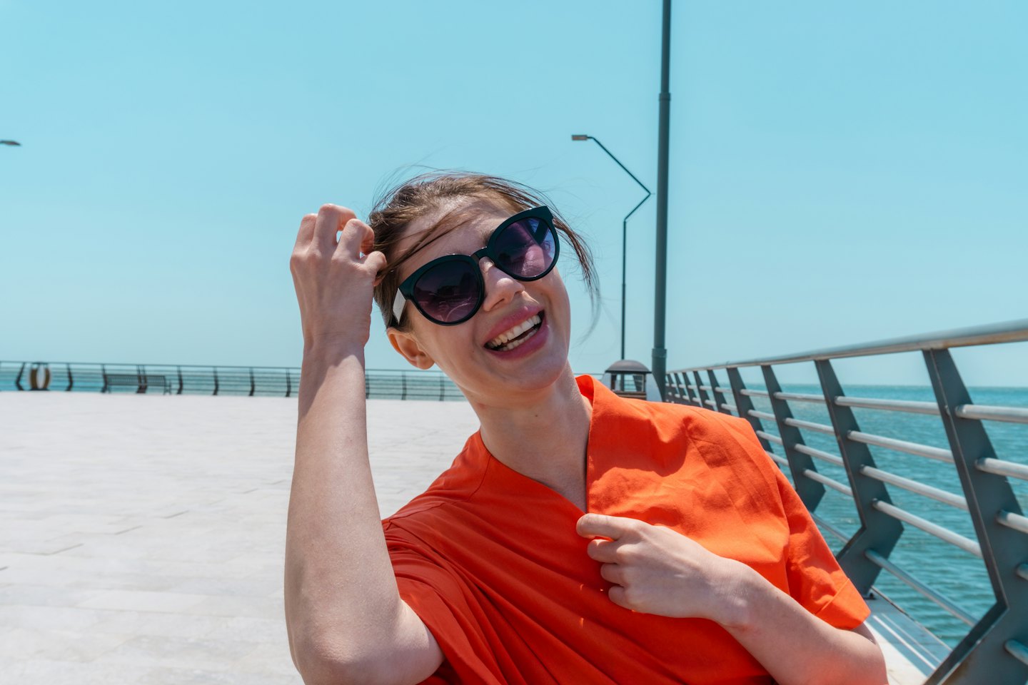Woman in orange shirt smiles while standing on a pier.